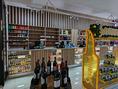 Bottle store POS and shelving: timber-slatted counter, lit glass bays, and back wall display—Gauteng